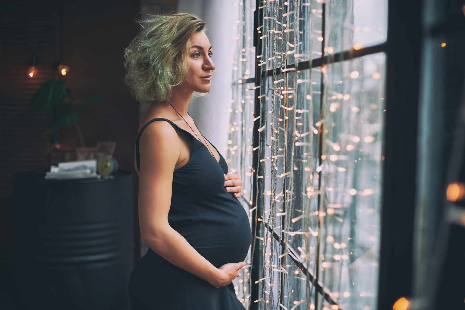 Junge schöne schwangere Frau steht am Fenster in einem Haus im Loftstil